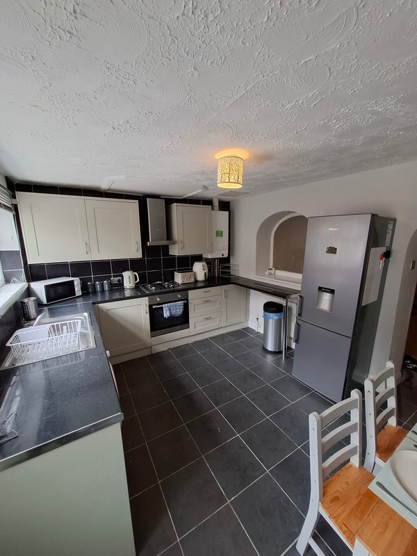 Modern kitchen with white cabinets, black countertops, stainless steel fridge and black tile flooring