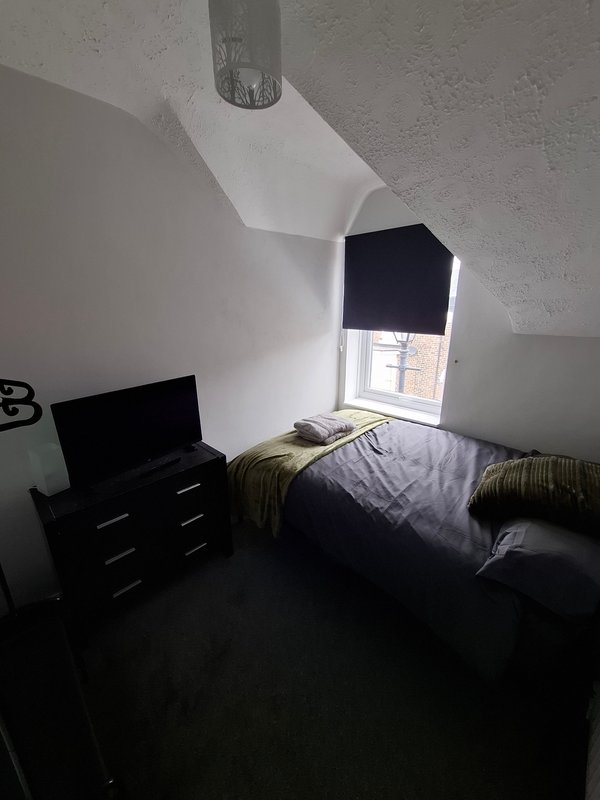 Small bedroom with single bed, black dresser, laptop, and window with blinds
