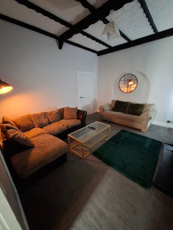 Modern living room with orange sectional sofa, wooden table, green rug and exposed beam ceiling