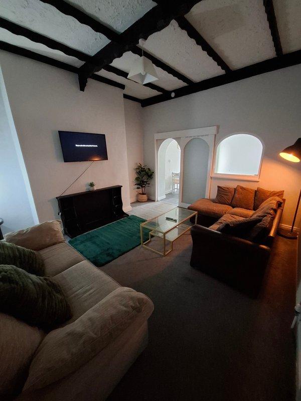 Open-plan living room with exposed beam ceiling, sofas, TV, and glass coffee table