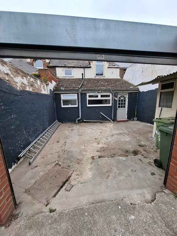 Paved courtyard with dark garage, white door, and residential building backdrop