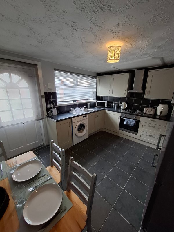 Kitchen and dining area with cream cabinets, black countertops, washing machine and dining table