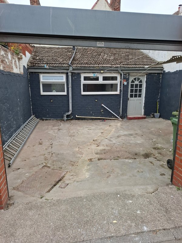 Dark blue single-story garage building with driveway and brick boundary walls