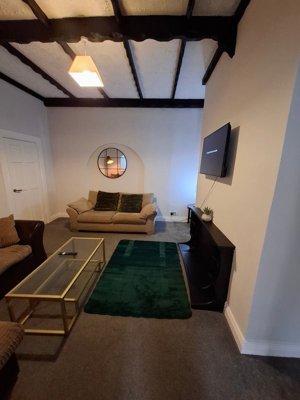 Modern living room with cream sofa, green rug, glass coffee table and wall-mounted TV