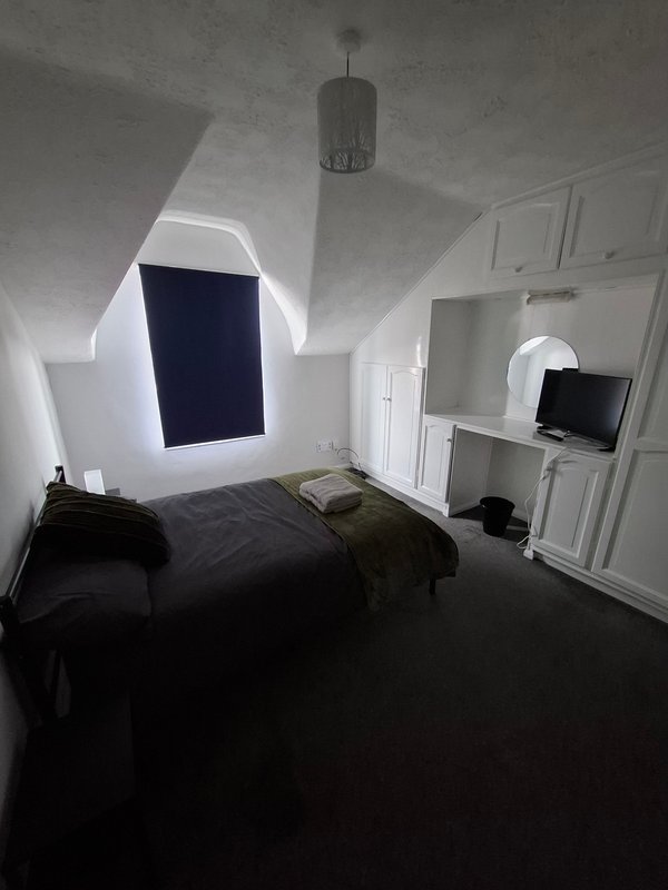Attic bedroom with sloped ceiling, dark bed, white wardrobe and window
