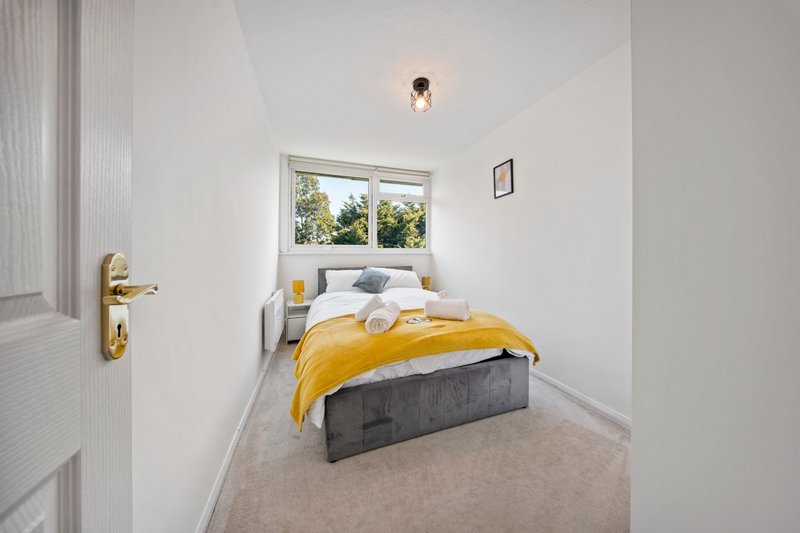 Bright modern bedroom with single bed, yellow throw, window overlooking garden, and cream carpet