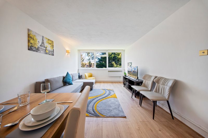 Open-plan living and dining room with wooden table, sofa, chairs, and window view