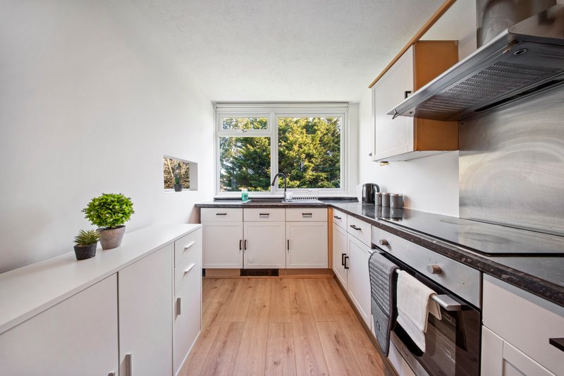 Modern galley kitchen with white cabinets, stainless steel appliances and wooden flooring