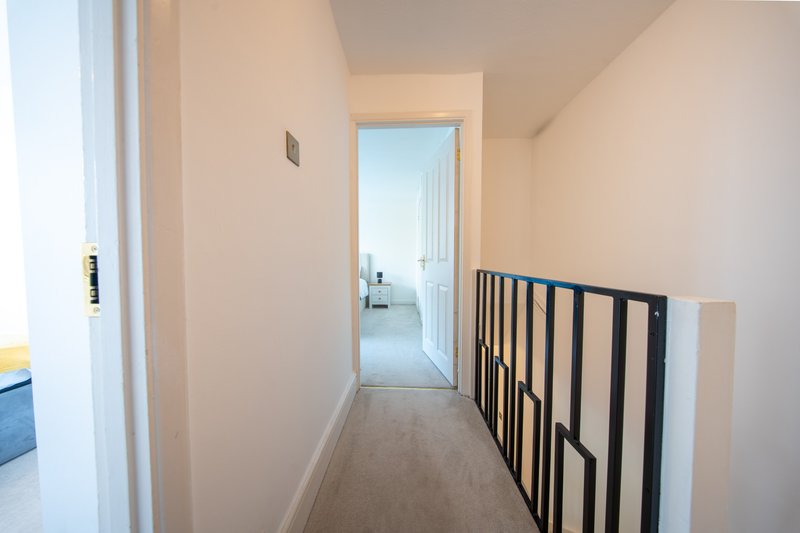 Hallway with beige walls, wooden flooring, black stair gate and open doorway to bedroom