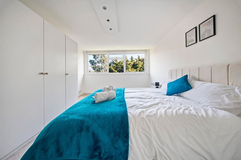 Bright bedroom with two single beds, blue and white bedding, white wardrobe and window with garden view