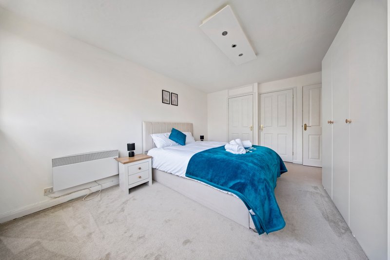 Bright bedroom with double bed, blue bedding, white wardrobes and neutral carpet