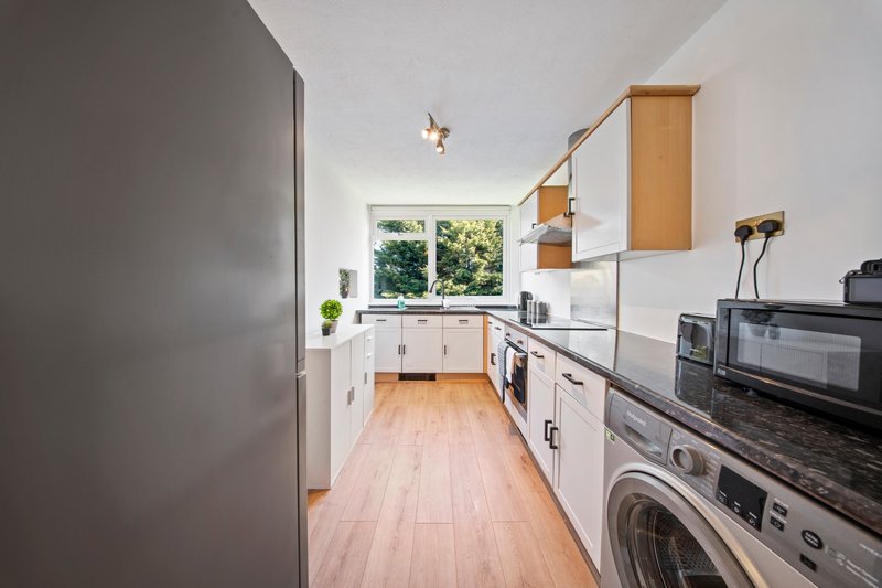 Modern galley kitchen with white cabinetry, wooden flooring, stainless steel appliances and window.