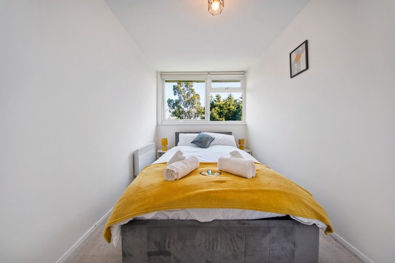 Bright bedroom with single bed, yellow throw, white pillows and window view of trees