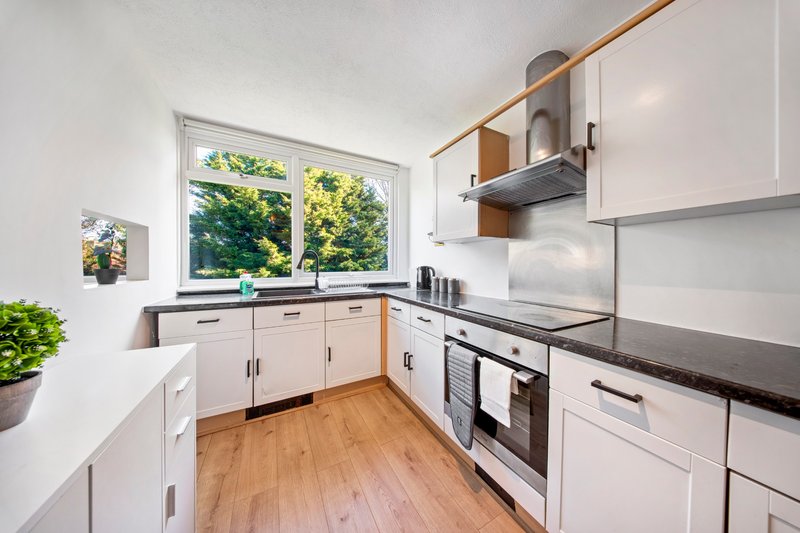Modern kitchen with white cabinetry, black countertops, stainless steel appliances and wooden flooring