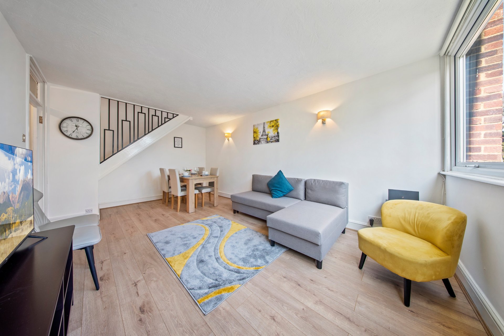 Open-plan living room with grey sofa, yellow armchair, dining table, and staircase to upper floor
