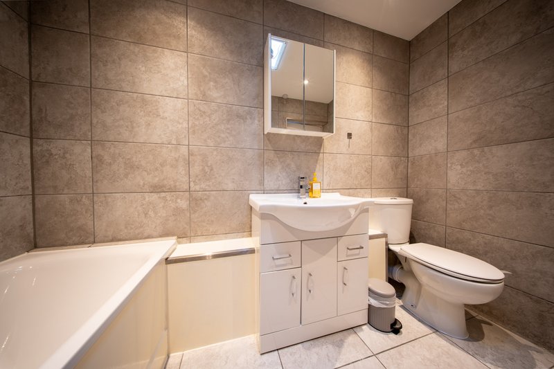 Modern bathroom with beige vanity, white sink, mirrored cabinet, bathtub and toilet