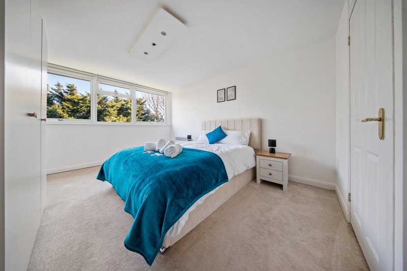 Bright bedroom with single bed, blue bedding, wooden nightstand and large window with garden views