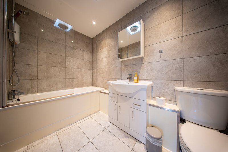 Modern bathroom with bathtub, white vanity sink, toilet, and illuminated mirror cabinet