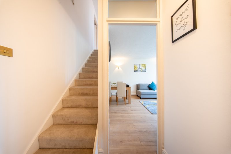 Staircase with beige carpet leading to bright open-plan living area with blue sofa