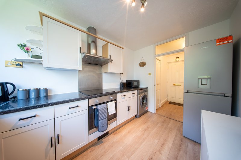 Modern kitchen with white cabinetry, stainless steel appliances, black countertop and wooden flooring