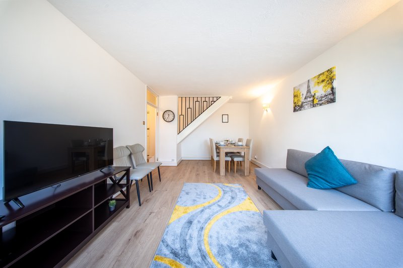 Open-plan living room with sofa, TV, dining table, and staircase to upper level