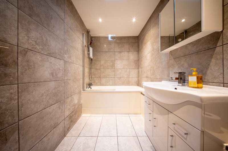 Modern bathroom with tiled walls, white vanity sink, mirror, bathtub and recessed lighting