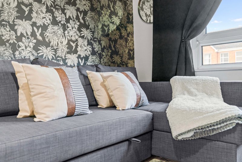 Modern living room with gray sofa, decorative pillows, throw blanket, and patterned wallpaper