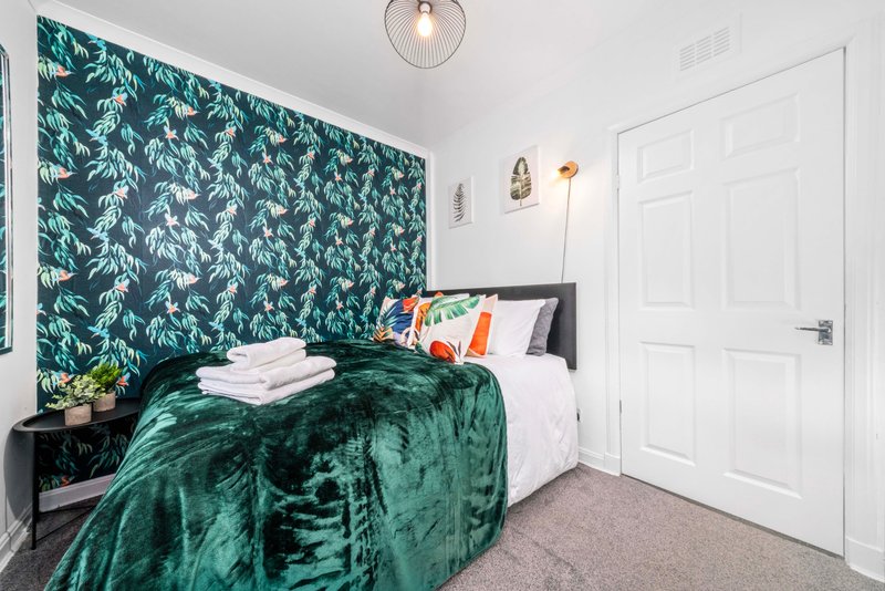 Modern bedroom with green velvet bedding, patterned wallpaper, white door and pendant light