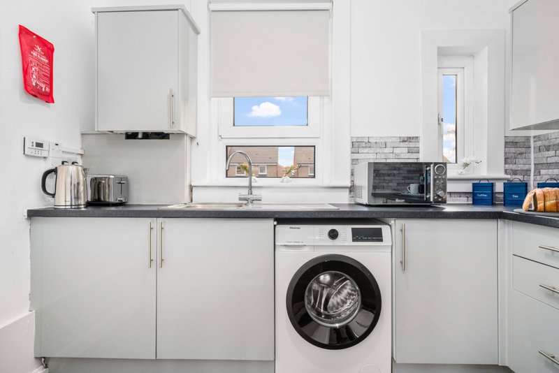 Modern white kitchen with washing machine, dark countertop, and window view