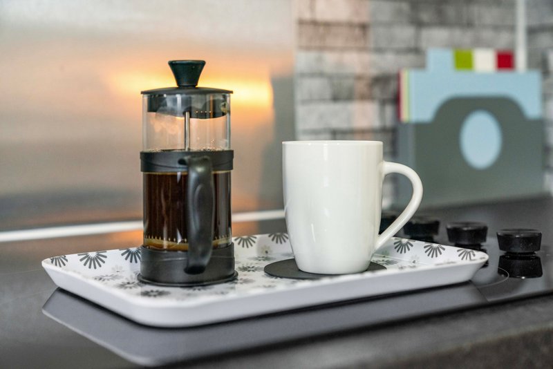 Coffee setup with French press, white mug, and tray on windowsill with sunset view