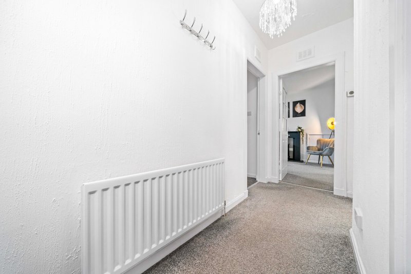Bright hallway with white walls, radiator, carpet flooring and open doorway to living area