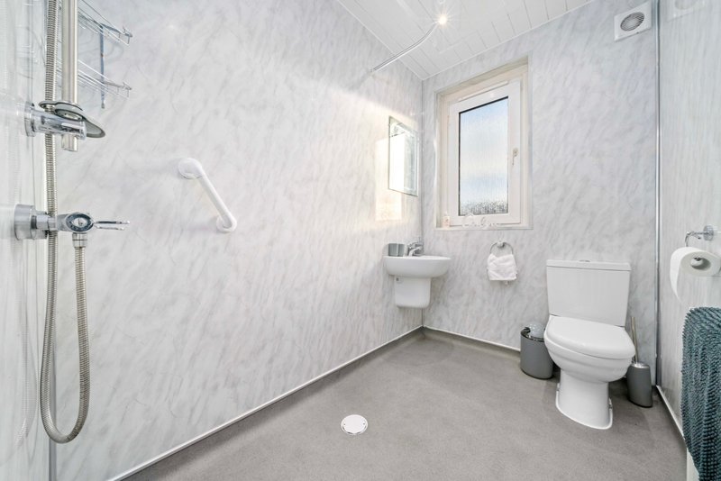 Modern bathroom with marble-effect tiled walls, toilet, sink, shower area and window