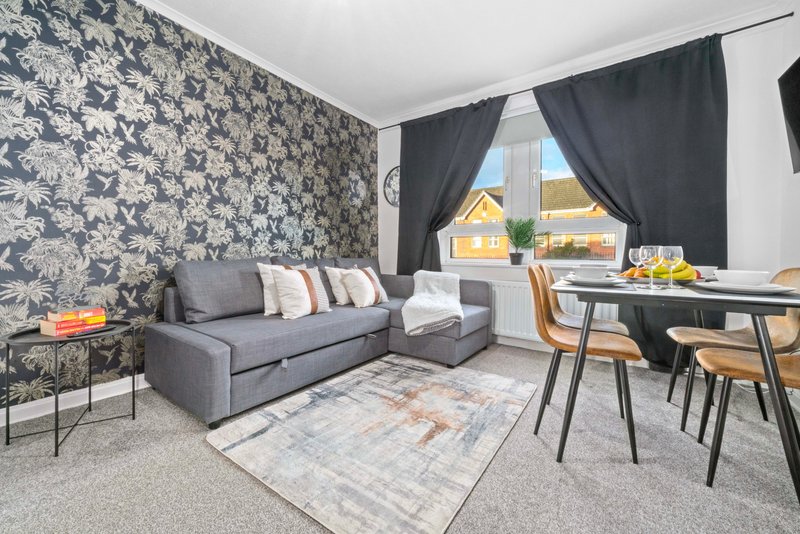 Modern living room with gray sofa, patterned wallpaper, dining table and large window with dark curtains