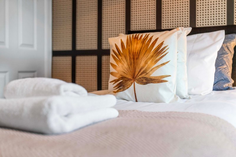 Bed with white pillows, decorative cushion with gold leaf pattern, and folded towels