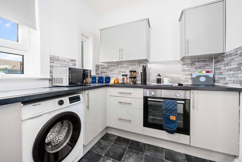 Modern kitchen with white cabinetry, black countertops, washing machine, oven and brick-patterned backsplash