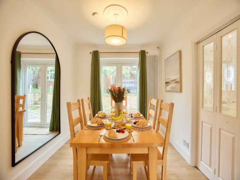 Bright dining room with wooden table, four chairs, set for meal, large mirror and garden views