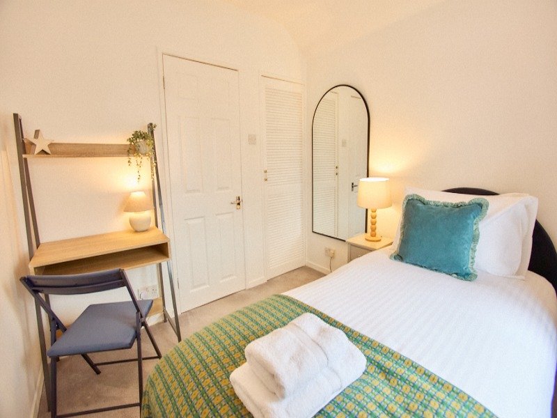 Bright bedroom with double bed, green striped rug, desk with chair and arched mirror