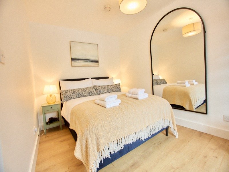 Modern bedroom with double bed, wooden flooring, arched mirror and bedside lighting