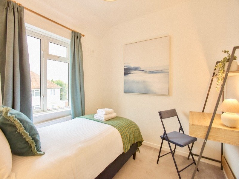 Bright bedroom with single bed, green throw, cushions, chair and window view