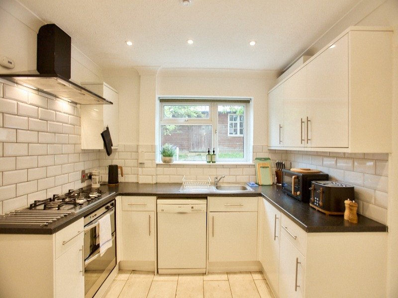 Modern cream kitchen with gas hob, oven, black worktops, subway tile splashback and garden view
