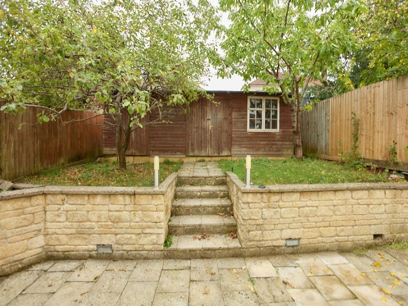 Garden with wooden cabin, raised stone walls, paved terrace and mature trees