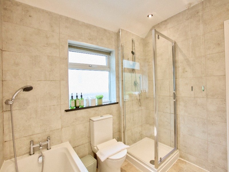 Modern bathroom with beige tile, glass shower enclosure, toilet and window with toiletries