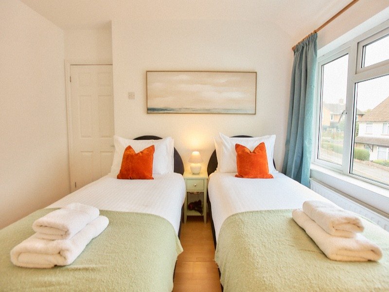 Twin bedroom with two single beds, orange cushions, bedside lamp and window view