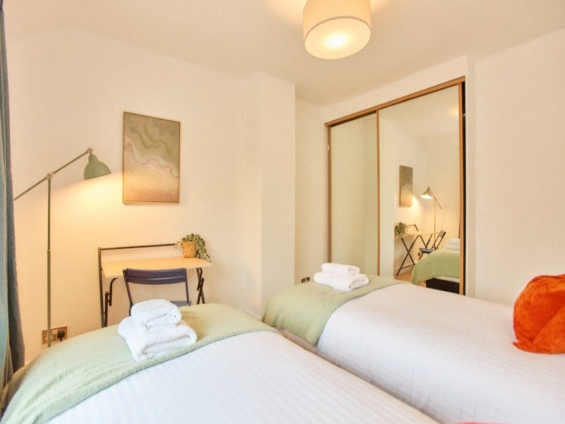 Modern bedroom with two single beds, mirrored wardrobe, wall art and ceiling light