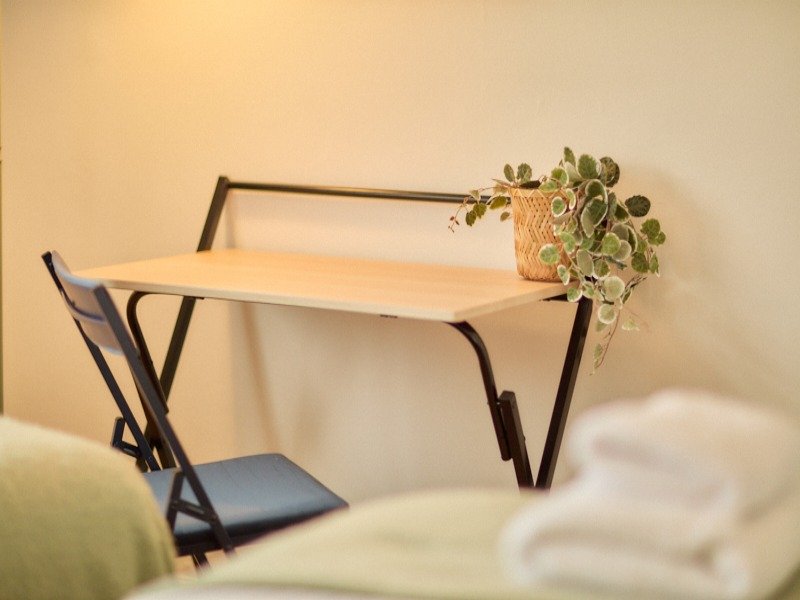 Minimalist desk with black metal frame, wooden top, potted plant, and folding chair