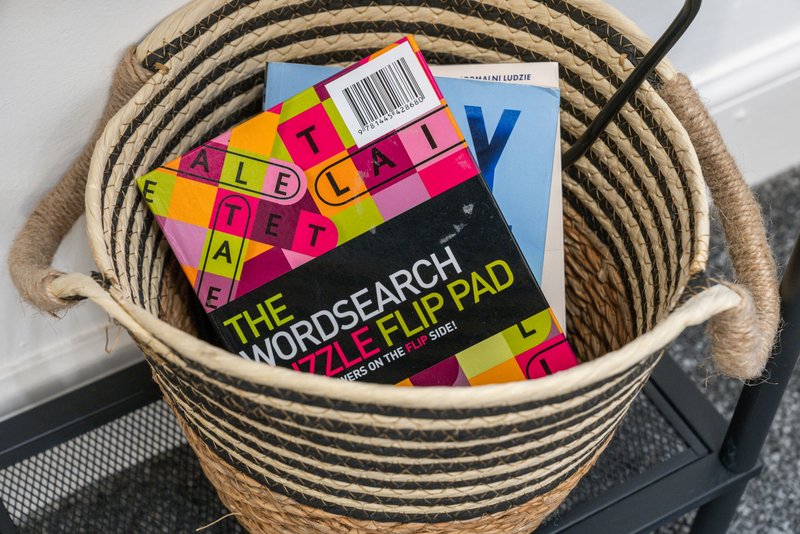 Woven rope basket containing colorful board games and books on dark floor