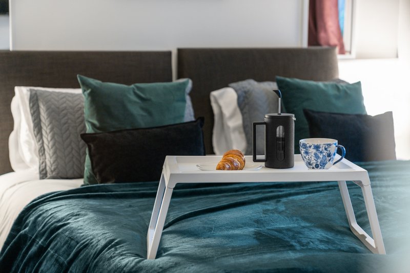 Bedroom with teal bedding, decorative pillows, white bed tray with coffee cup and croissant