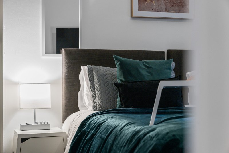 Modern bedroom with dark teal bedding, gray upholstered headboard, and white bedside lamp