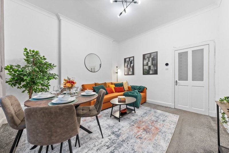 Open-plan living and dining area with orange sofa, round dining table, and potted plants