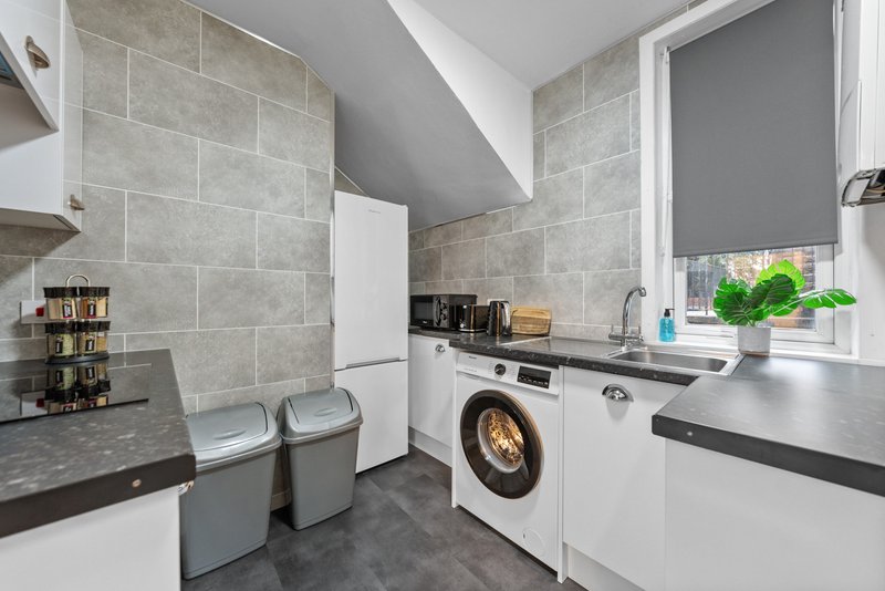 Modern kitchen with white appliances, gray tile walls, black countertops and washing machine